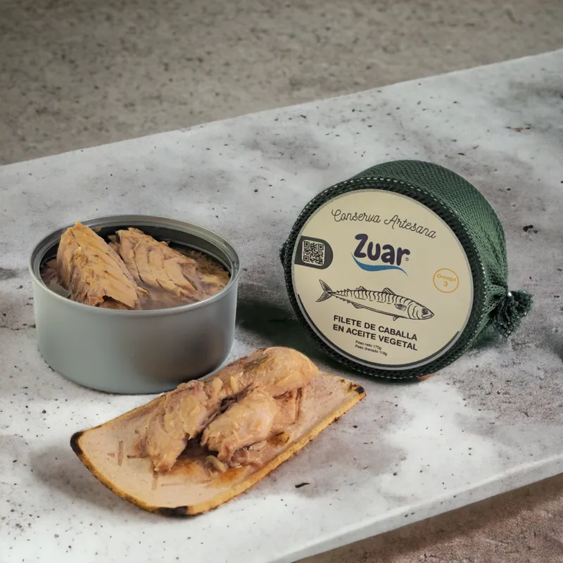 Open can of ZUAR mackerel fillet in vegetable oil next to its green-mesh pack, on marble.